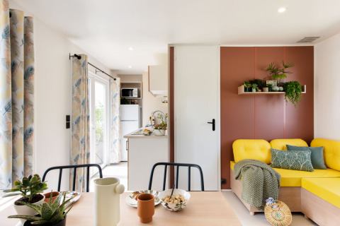Heller Wohnbereich im Stacaravan Confort PLUS mit gelbem Sofa, Pflanzen und moderner Küche in Frankreich.