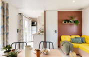 Lichte, moderne leefruimte in Stacaravan Confort PLUS met gele bank en planten op Franse camping.