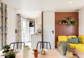 Lichte, moderne leefruimte in Stacaravan Confort PLUS met gele bank en planten op Franse camping.