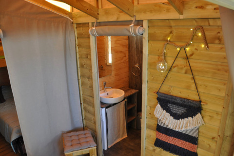 Knus boomhuissinterieur met houten wanden, badkamer en wanddecoratie op Flower Camping Au Bois Des Biches, Frankrijk.
