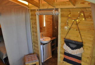 Knus boomhuissinterieur met houten wanden, badkamer en wanddecoratie op Flower Camping Au Bois Des Biches, Frankrijk.