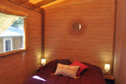 Gezellige houten slaapkamer met tweepersoonsbed, kussens, lampjes en spiegel in een boomhut in Frankrijk.