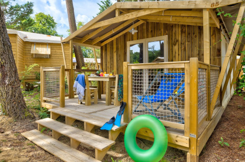 Holzhütte mit Veranda, blauen Liegestühlen und Schwimmring im Sweetflower-Lodge bei Flower Camping Au Bois Des Biches in Frankreich.