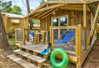 Holzhütte mit Veranda, blauen Liegestühlen und Schwimmring im Sweetflower-Lodge bei Flower Camping Au Bois Des Biches in Frankreich.