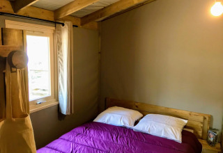 Gezellige slaapkamer met houten balken, tweepersoonsbed met paarse deken en raam in Sweetflower Lodge.
