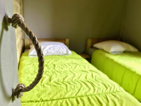 Zwei Einzelbetten mit limettengrüner Bettwäsche in der Sweetflower-Lodge bei Flower Camping Au Bois Des Biches, Frankreich.