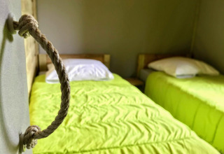 Twee eenpersoonsbedden met limoengroene dekens in Sweetflower-lodge bij Flower Camping Au Bois Des Biches, Frankrijk.