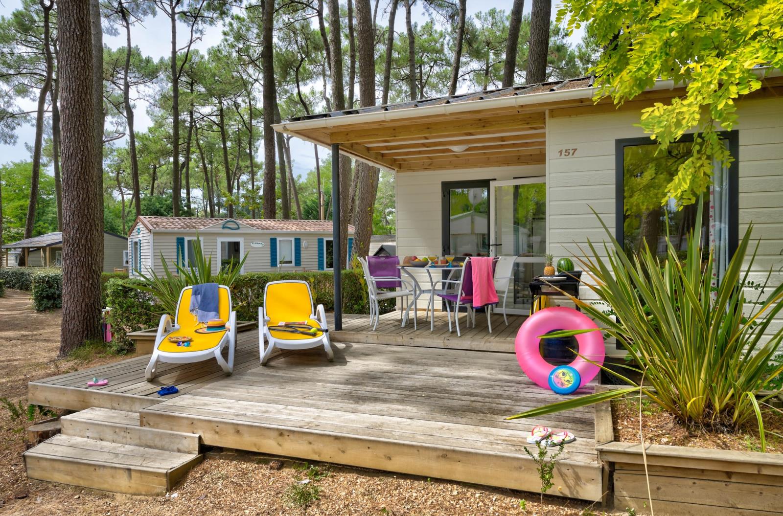 Buitenterras met ligstoelen en eettafel bij Cottage Premium van Flower Camping Au Bois Des Biches in Frankrijk.