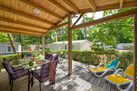 Terrazza coperta presso Cottage Premium, Flower Camping Au Bois Des Biches, Francia, con tavolo e lettini.