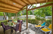 Terraza cubierta en Cottage Premium de Flower Camping Au Bois Des Biches, Francia, con mesa y tumbonas.