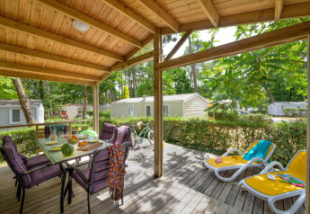 Terraza cubierta en Cottage Premium de Flower Camping Au Bois Des Biches, Francia, con mesa y tumbonas.