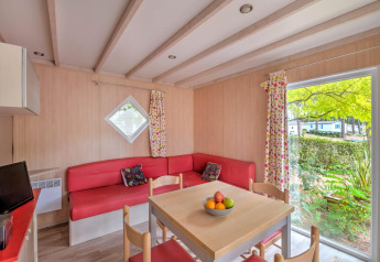 Interior de cabaña moderna con sofá rojo, mesa de comedor y ventanal en Flower Camping Au Bois Des Biches, Francia.