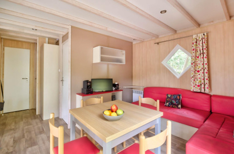 Interno del Cottage Premium presso Flower Camping Au Bois Des Biches, Francia, con divani rossi e tavolo.