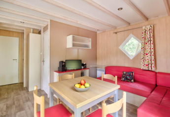 Interior de la cabaña Cottage Premium en Flower Camping Au Bois Des Biches, Francia, con sofás rojos y mesa.