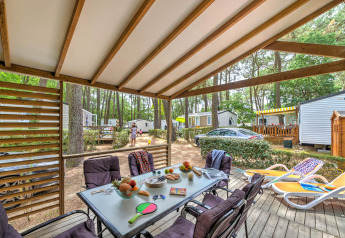 Terraza cubierta en Cottage Premium de Flower Camping Au Bois Des Biches en Francia, con mesa y tumbonas.