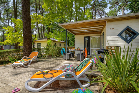 Solrig terrasse med liggestole foran Cottage Premium, Flower Camping Au Bois Des Biches, omgivet af træer.