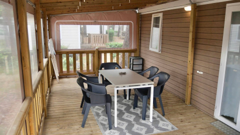 Véranda couverte avec table, six chaises noires et tapis dans un chalet au Flower Camping Au Bois Des Biches.