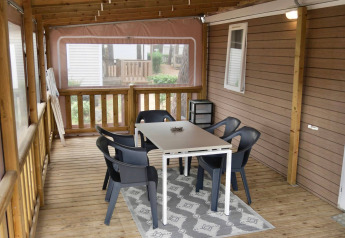 Überdachte Terrasse mit Tisch, sechs schwarzen Stühlen und Teppich bei einem Chalet im Flower Camping Au Bois Des Biches.