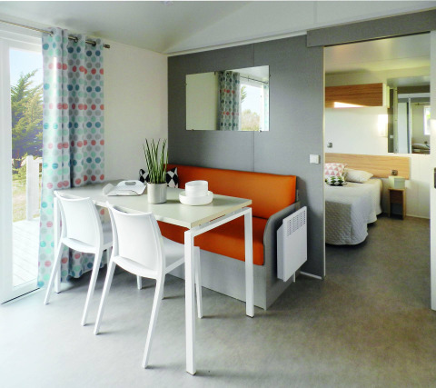 Modern Stacaravan Life chalet with dining table, orange bench, and bedroom view at Flower Camping Au Bois Des Biches, France.