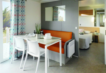 Modern Stacaravan Life chalet with dining table, orange bench, and bedroom view at Flower Camping Au Bois Des Biches, France.