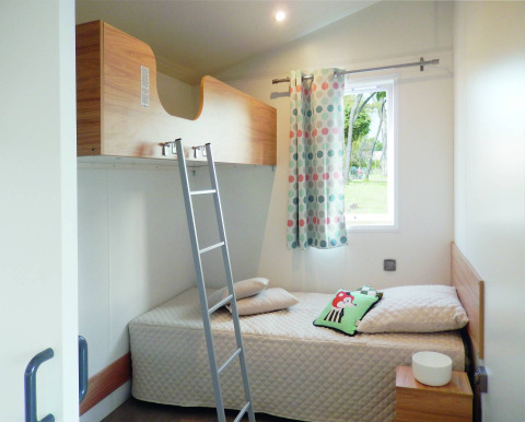 Stanza luminosa allo Stacaravan Life al Flower Camping Au Bois Des Biches con letti a castello e tenda colorata.