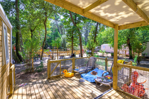 Zonnig terras bij Stacaravan Family op Flower Camping Au Bois Des Biches, tussen de bomen en chaletjes.