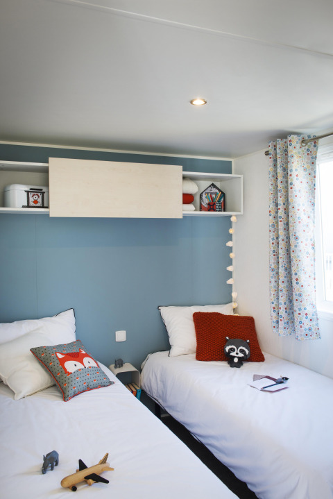 Kinderkamer met twee aparte bedden, kleurrijke kussens en speelgoed in Stacaravan Family, Flower Camping Au Bois Des Biches.