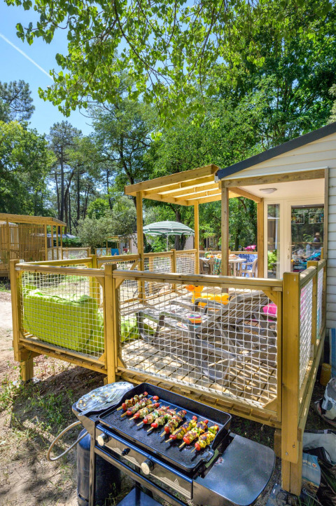 Terrazza esterna di uno chalet con spiedini alla griglia, immersa nel verde bosco in Francia.