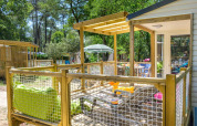 Holzterrasse mit Grillspießen an einem Chalet, umgeben von Wald bei sonnigem Wetter in Frankreich.