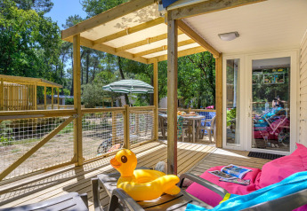 Wooden terrace with inflatable duck, lounge chair and outdoor dining at Stacaravan Family, Flower Camping Au Bois Des Biches, France.