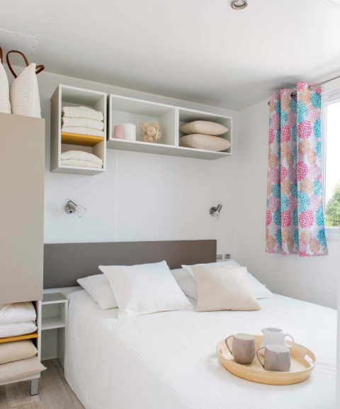 Dormitorio de chalet moderno con decoración clara, cama doble, estantes abiertos y cortinas coloridas en Francia.