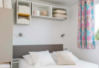 Dormitorio de chalet moderno con decoración clara, cama doble, estantes abiertos y cortinas coloridas en Francia.