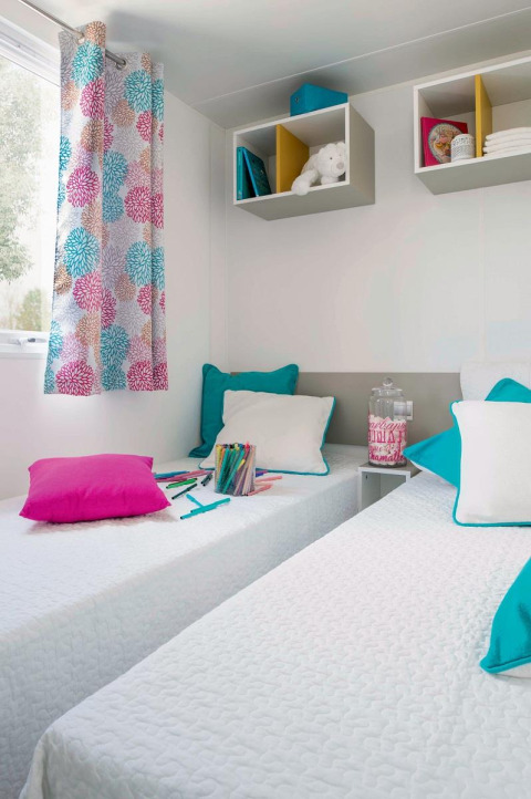 Due letti singoli con cuscini colorati in una stanza luminosa allo chalet Stacaravan Family, Flower Camping Au Bois Des Biches, Francia.