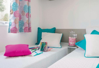 Due letti singoli con cuscini colorati in una stanza luminosa allo chalet Stacaravan Family, Flower Camping Au Bois Des Biches, Francia.