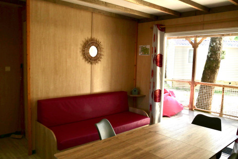 Binnenzicht van Cottage Family in Flower Camping Au Bois Des Biches met rode sofa en houten tafel.