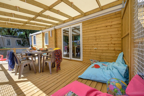 Wooden terrace with dining table, chairs and beanbags at Stacaravan Family, Flower Camping Au Bois Des Biches, France.