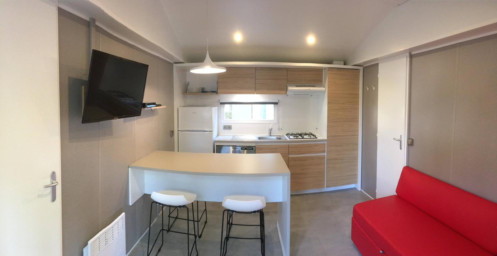 Interieur van Stacaravan Premium+ chalet bij Flower Camping Au Bois Des Biches met moderne keuken en rode bank.