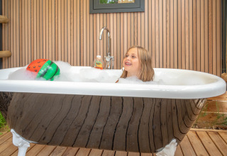 Kind geniet van een schuimbad in buitenbadkuip bij Stacaravan Garden op Flower Camping Au Bois Des Biches in Frankrijk.