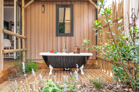 Kind sitzt in einer Badewanne auf der Holzterrasse, umgeben von Pflanzen, bei Stacaravan Garden, Frankreich