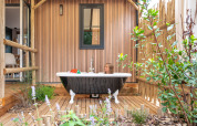 Enfant dans une baignoire extérieure sur terrasse en bois, entouré de plantes, au Stacaravan Garden, France