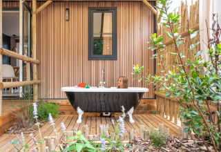 Kind in een buitenbad op houten terras met planten bij Stacaravan Garden, Flower Camping Au Bois Des Biches, Frankrijk