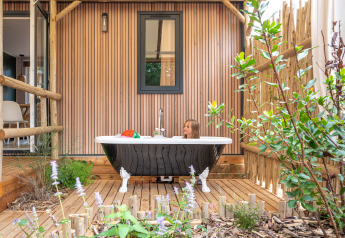 Enfant dans une baignoire extérieure sur terrasse en bois, entouré de plantes, au Stacaravan Garden, France