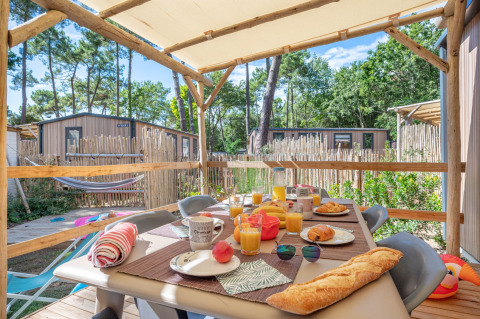 Überdachte Terrasse mit Frühstückstisch am Stacaravan Garden im Flower Camping Au Bois Des Biches, Frankreich.