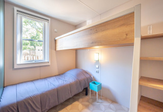 Bright single room at Stacaravan Garden with simple bed and window, Flower Camping Au Bois Des Biches, France.