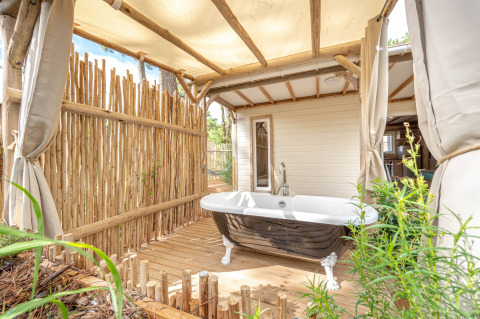 Bañera al aire libre en terraza de madera con valla de bambú en Cottage Garden, Flower Camping Au Bois Des Biches, Francia.