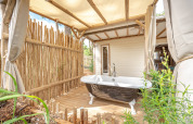 Freistehende Badewanne auf Holzterrasse mit Bambuszaun im Cottage Garden, Flower Camping Au Bois Des Biches, Frankreich.