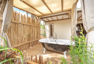 Bañera al aire libre en terraza de madera con valla de bambú en Cottage Garden, Flower Camping Au Bois Des Biches, Francia.