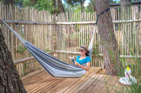 Mujer leyendo un libro en una hamaca sobre tarima de madera en Cottage Garden, Flower Camping Au Bois Des Biches, Francia.
