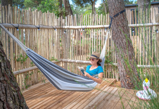 Mujer leyendo un libro en una hamaca sobre tarima de madera en Cottage Garden, Flower Camping Au Bois Des Biches, Francia.