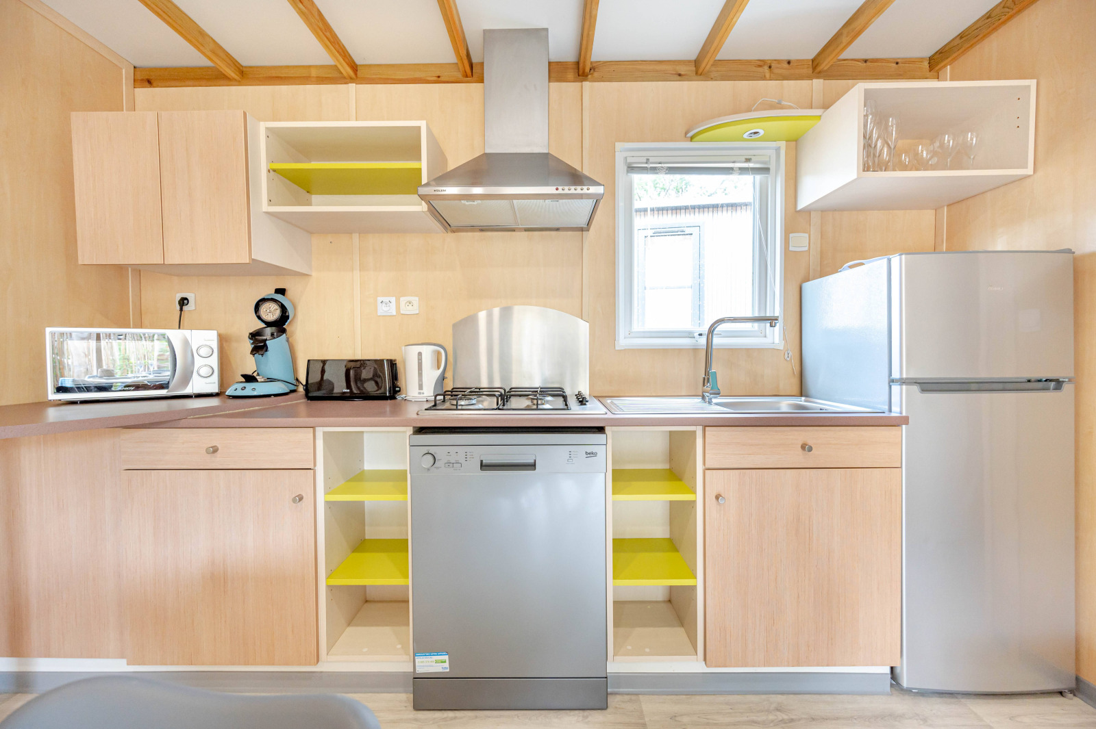Moderne keuken met houten kasten, vaatwasser, gootsteen, koelkast en kleine keukenapparaten.